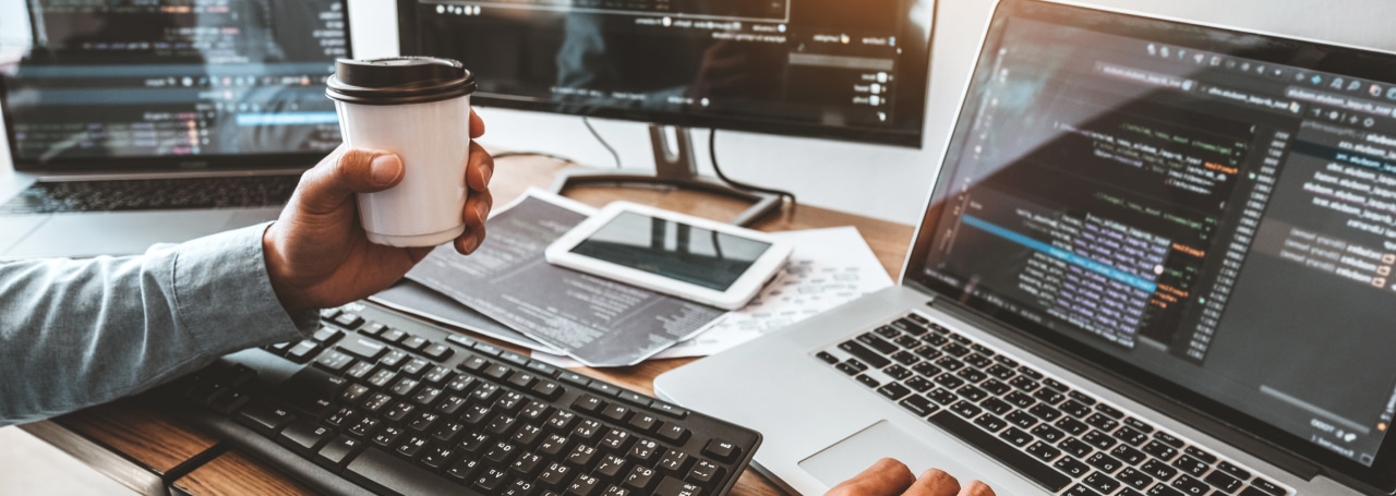 Coder with coffee and multiple screens
